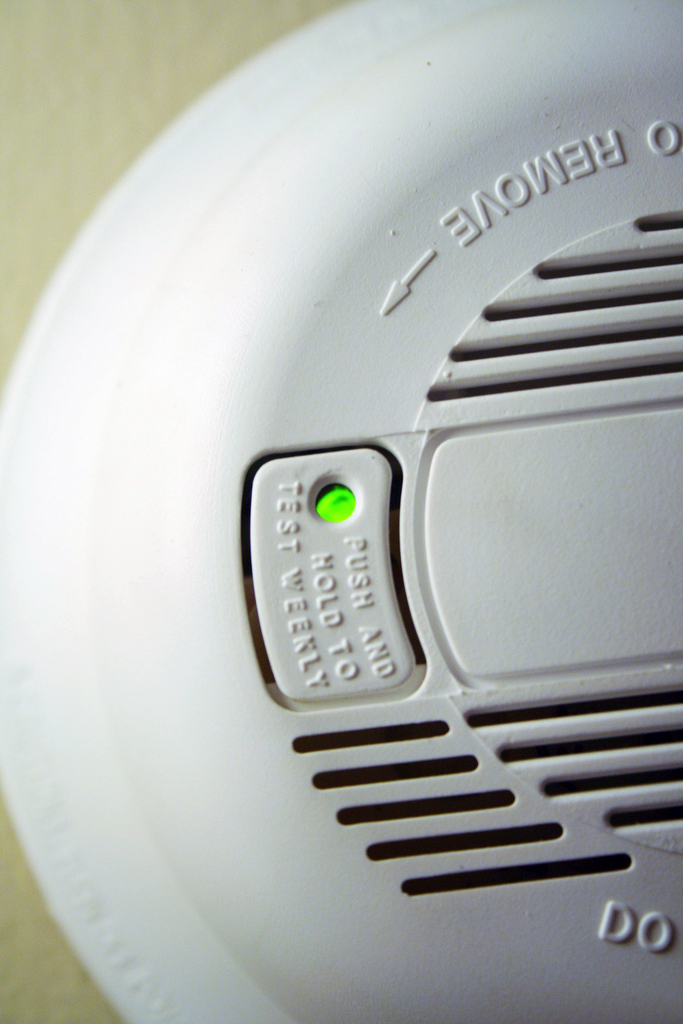 A smoke alarm with a green "test" button. 