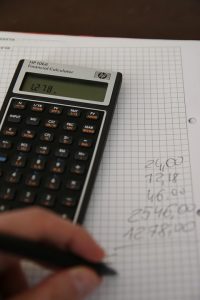 Someone using a calculator, paper, and pen to add numbers.