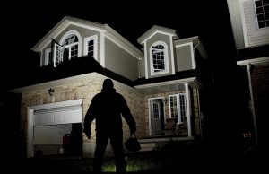 A burglar standing outside a well-lit house