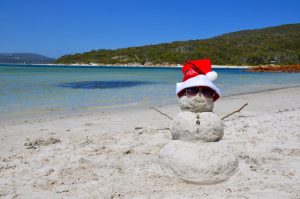 A "snowman" made out of sand on a beach with a santa hat.
