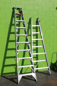 Two ladders leaning against a green cement wall.