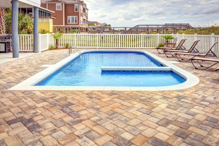 A fenced-in pool with a stone patio.