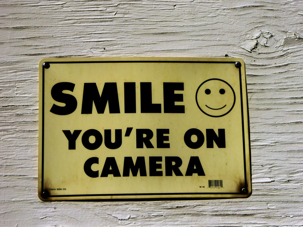 A yellow sign reading "SMILE YOU'RE ON CAMERA."