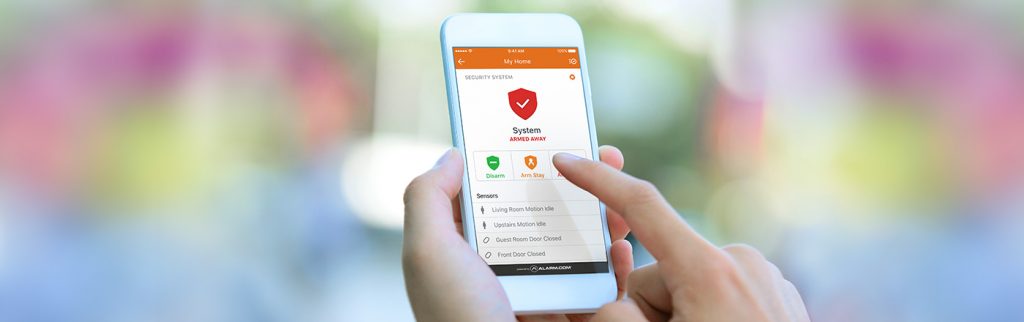 A hand holding a phone open to the Alarm.com app