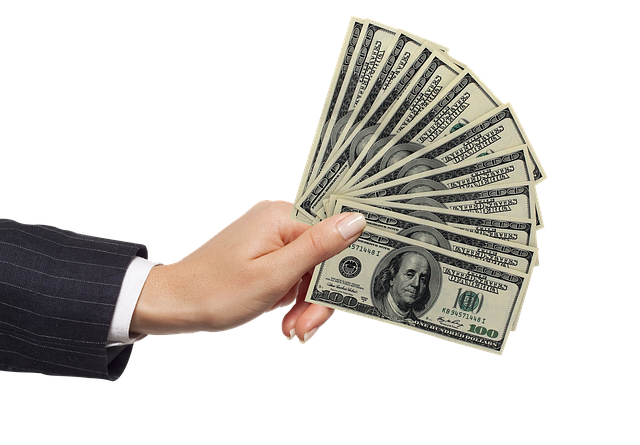A hand in a suit sleeve holding several $100 bills