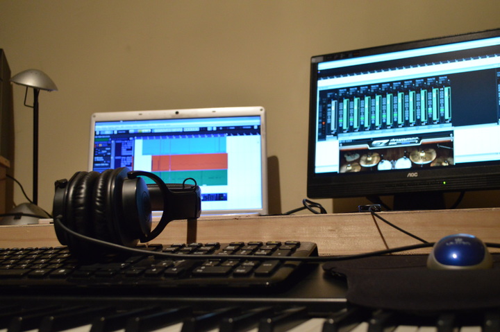 A keyboard, a pair of headpones, and computer monitors open to music mixing programs. 